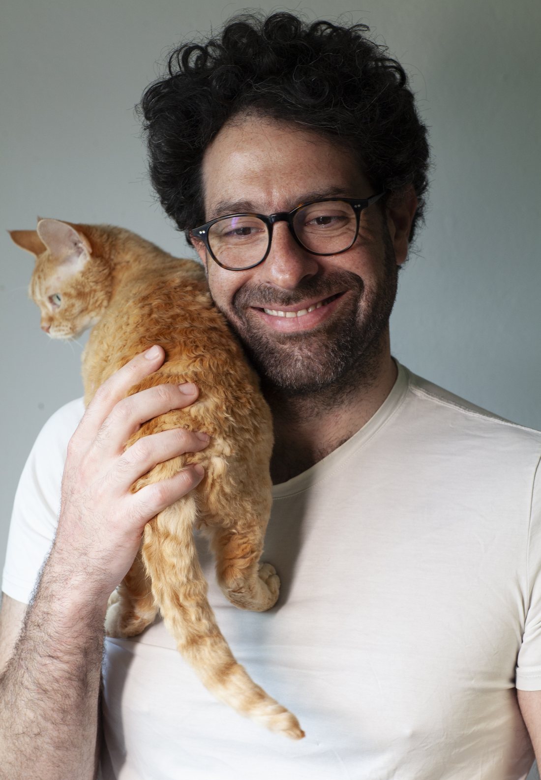Ayham Kader, leaning against a pale wall in a green corduroy shirt.