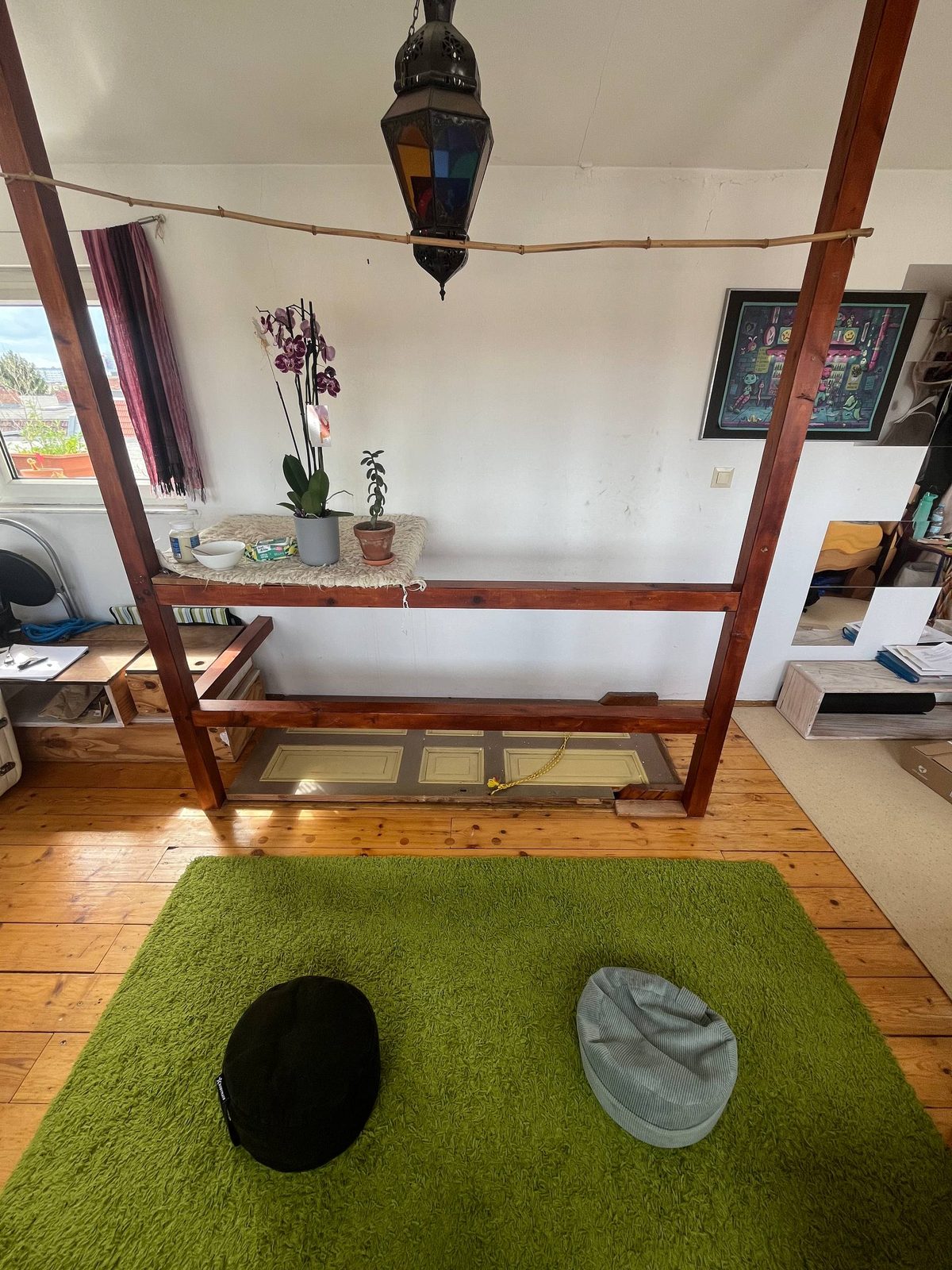 The meditation corner: cushions on a green rug beneath a wooden frame and a lantern.